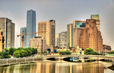 Modern buildings by river against sky in city