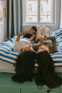 Young female friends using smart phone while lying on bed at home