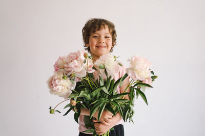 Cheerful happy child with peonys bouquet. smiling little boy on white background.