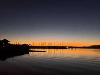 Silhouette buildings by lake against sky during sunset