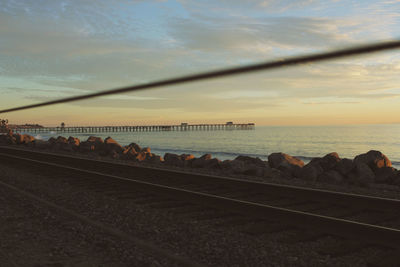 Railroad tracks by sea against sky during sunset
