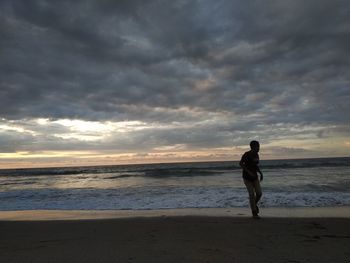 Full length of man standing on beach against sky during sunset