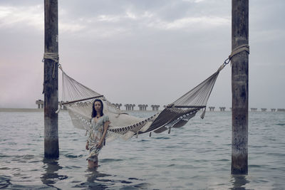 Woman standing in sea against hammock