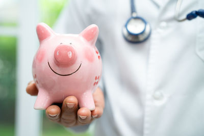 Midsection of doctor holding piggy bank