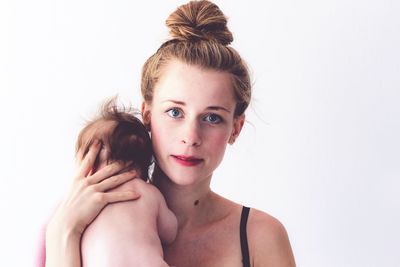 Portrait of mother carrying shirtless daughter against white background