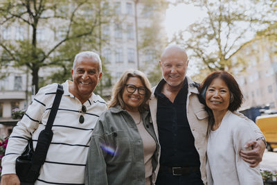 Portrait of smiling elderly male and female friends standing with arms around at street
