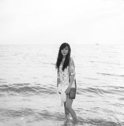 Portrait of young woman standing on beach against clear sky