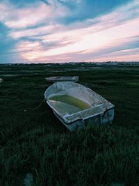 Abandoned car on field against sky during sunset