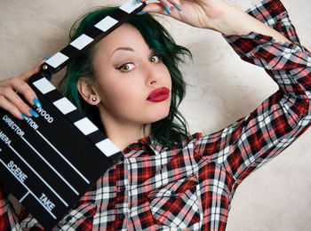 Portrait of young woman holding film slate against wall