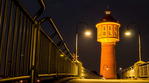 Illuminated bridge leading towards tower at night