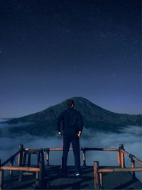 Rear view of man standing on mountain against sky