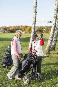 Full length of senior female friends choosing golf club on golf course