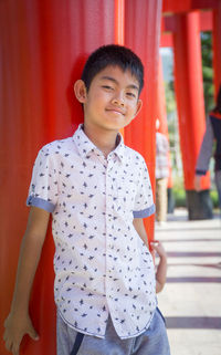 Portrait of smiling boy standing against red torii
