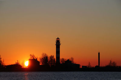 Silhouette lighthouse by sea against clear sky during sunset