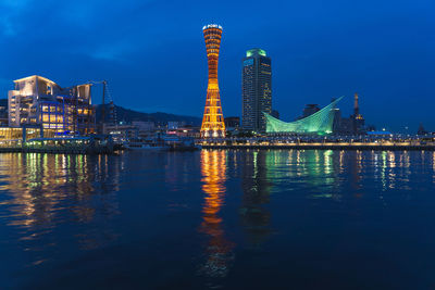 Illuminated modern buildings by river against sky at night