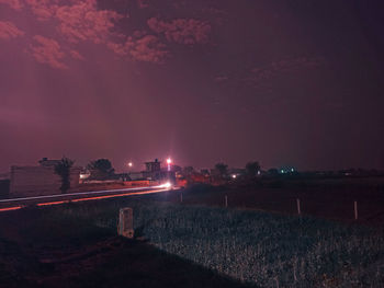 Illuminated road amidst field against sky at night