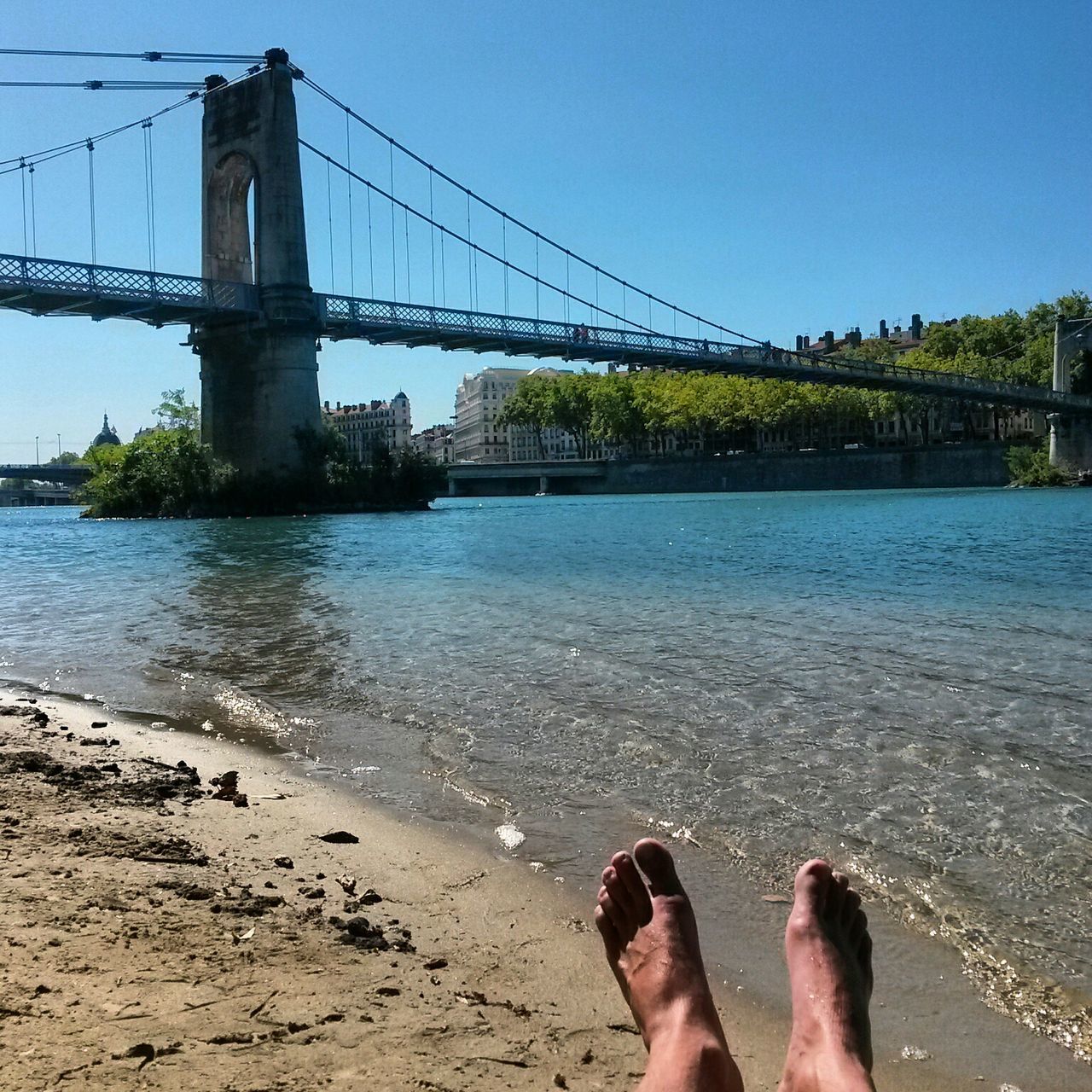 water, connection, low section, person, built structure, bridge - man made structure, clear sky, architecture, sea, blue, personal perspective, bridge, river, engineering, leisure activity, lifestyles, suspension bridge