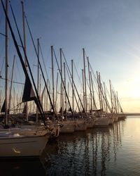 Sailboats moored in sea against sky during sunset