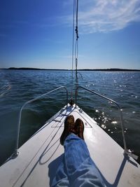 Low section of man on sailboat sailing in sea against sky