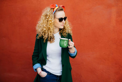 Young woman wearing sunglasses standing against wall