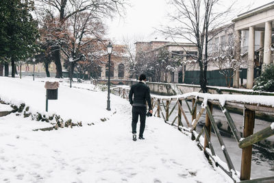 Rear view of man walking on snow covered footpath during winter