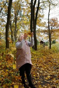 Full length of woman standing amidst trees in forest during autumn