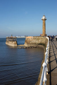 Lighthouse by sea against clear sky