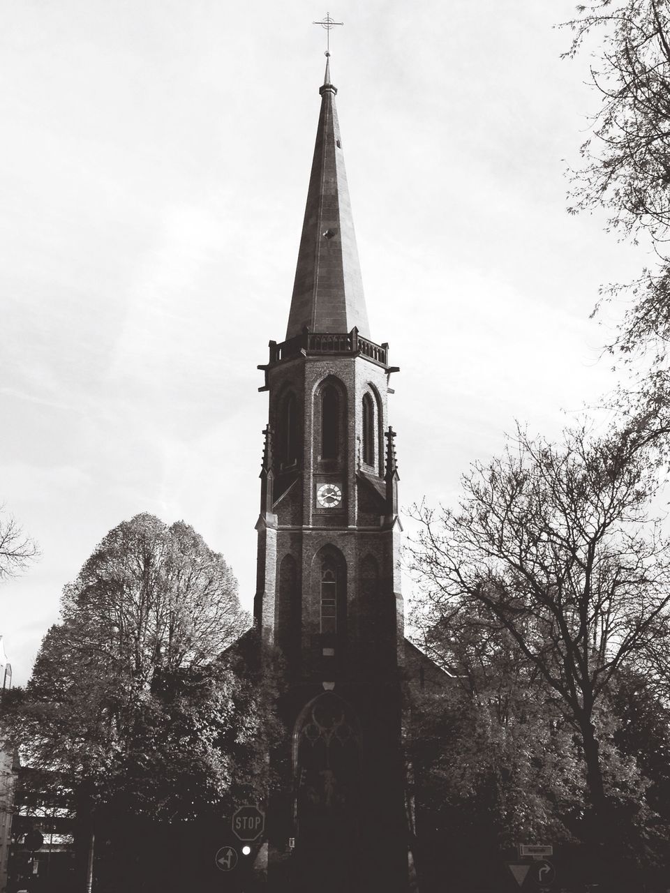 low angle view, tree, architecture, building exterior, built structure, religion, place of worship, church, spirituality, tower, sky, tall - high, clock tower, cross, steeple, history, branch, outdoors