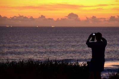 Man photographing sunset over sea