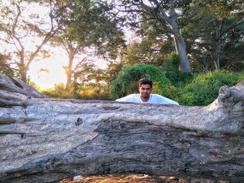 Portrait of young man by fallen tree trunk in forest