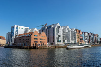 Buildings by river against clear blue sky