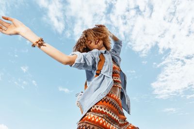 Rear view of woman with arms outstretched against sky