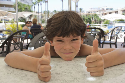 Portrait of boy showing thumbs up while sitting at table