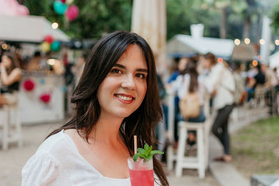 Beautiful young woman drinking strawberry mojito cocktail in park in city