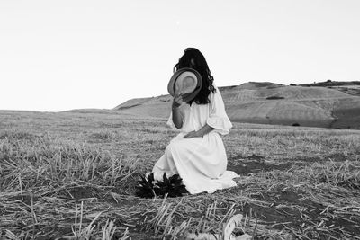 Woman covering face with hat on land against clear sky