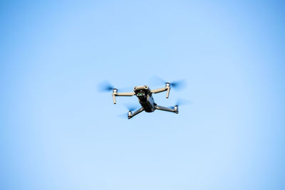 Low angle view of drone flying against clear blue sky