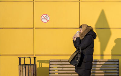 Side view of young woman standing against yellow wall