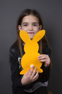 Portrait of smiling girl holding paper eater bunny against gray background