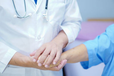 Midsection of doctor holding hands with female patient in hospital