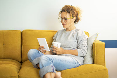 Young woman using phone while sitting on sofa at home