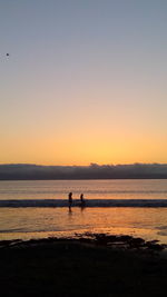 Silhouette people on beach against clear sky during sunset