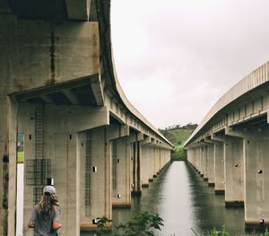 Rear view of woman standing amidst bridge over river against sky