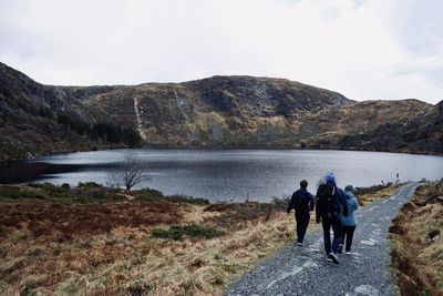 Rear view of people by lake against sky