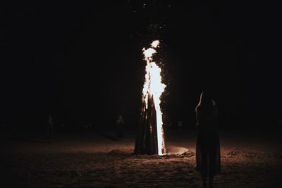 Rear view of woman standing by camp fire on beach