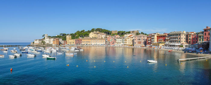 Sailboats in city by sea against clear blue sky