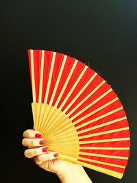 Cropped hand of woman holding folding fan against black background