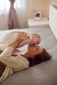 Young mother with red hair is lying on the bed with her daughter at home in the morning