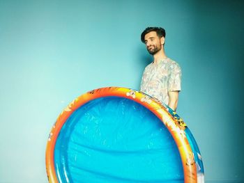 Confused young man holding wading pool against blue background