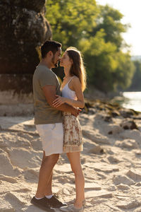 Side view of young couple embracing while standing on sand