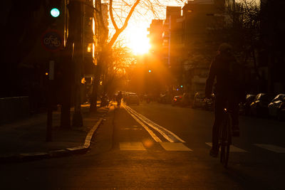 Rear view of man cycling on city street at sunset